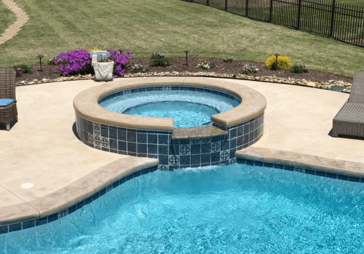 A close-up on a spa with a waterfall attached to a swimming pool. The spa is made of concrete with decorative tile on the exterior. Built in South Carolina