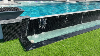 A black concrete pool with an infinity edge and fire bowls.
