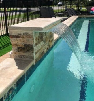 A close-up of a cascade water feature. The water falls in a smooth sheet into the pool.